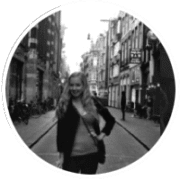 A person stands on a cobblestone street lined with buildings and bicycles, resembling typical Amsterdam architecture. The atmosphere is lively and urban.