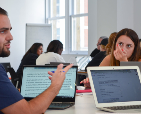 A group of people engaged in discussion around laptops in a bright, modern room. Collaboration and focus are evident.