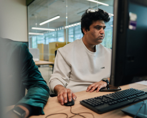 Two people working intently at computer screens in a modern office environment with glass walls and bright lighting.