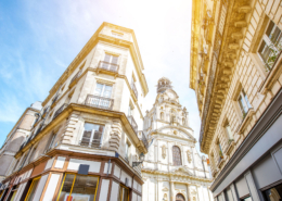 Historic cityscape with classic Parisian architecture, featuring Église Sainte-Élisabeth de Hongrie's ornate facade under a bright sky, framed by urban buildings.