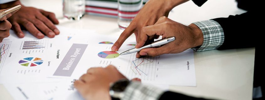 People reviewing business reports with charts and graphs at a meeting table, focusing on data analysis and collaborative decision-making.