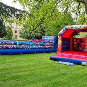 Inflatable bounce houses labeled "Party Time" are set up on grass, surrounded by tall trees and historical building in the background.