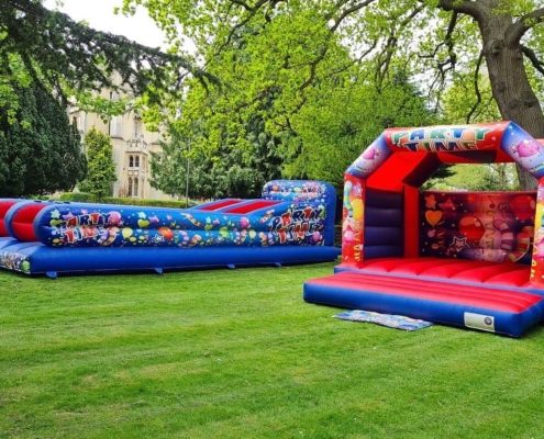 Inflatable bounce houses labeled "Party Time" are set up on grass, surrounded by tall trees and historical building in the background.