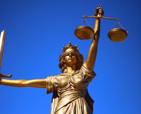 Golden Lady Justice statue holding scales and sword against a clear blue sky, symbolizing fairness and law.