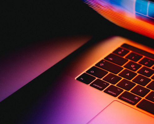 Close-up of a laptop keyboard with vibrant, colorful reflections on the screen, creating a dynamic and modern visual effect.