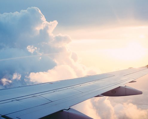 An airplane wing against a backdrop of fluffy clouds and a vibrant sunset, seen from a passenger's perspective in the sky.