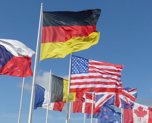 A collection of international flags, including Germany, USA, and Canada, waving against a clear blue sky, symbolizing global unity and diversity.