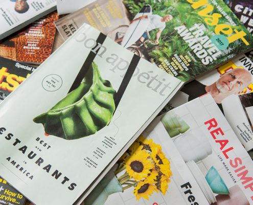 A variety of magazines are scattered, including Bon Appétit, Sunset, Outside, and Real Simple, featuring diverse themes and eye-catching covers.