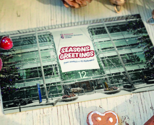 A seasonal greetings card featuring Richmond American University London, adorned with festive decorations, pinecones, and a heart-shaped gingerbread cookie.