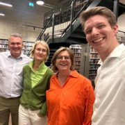 Four people smiling together in a library, surrounded by bookshelves and a staircase, capturing a candid, cheerful moment indoors.