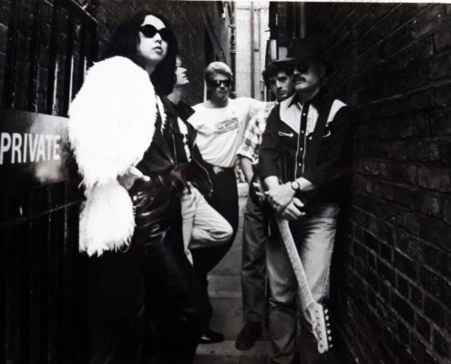 Five people stand in a narrow alleyway, one holding a guitar. "Private" sign visible on a door, monochrome setting.
