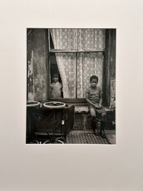 A black and white room is filled with furniture, a window, a picture frame, a chair, photographic paper, and art, creating a monochrome atmosphere.