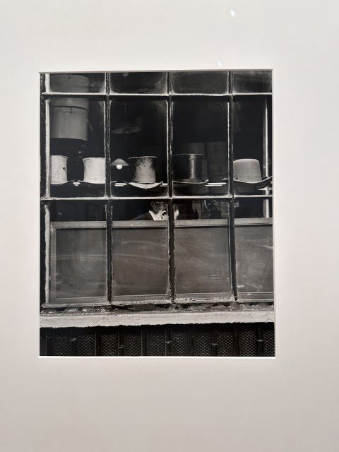 A black and white rectangular piece of art hangs in the window of an indoor room.