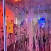 A person in a neon-lit room with paint splatters on glass, creating an abstract and colorful ambiance.
