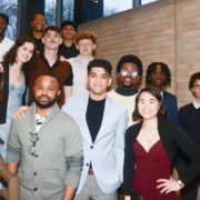 A group of diverse people smiling for a photo on a staircase, dressed in smart casual attire, suggesting a social or semi-formal event.