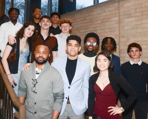 A group of diverse people smiling for a photo on a staircase, dressed in smart casual attire, suggesting a social or semi-formal event.