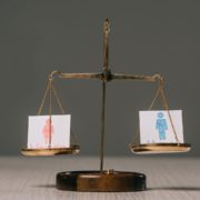 A traditional balance scale with two drawings representing people, one pink and one blue, suggesting a concept of gender equality or comparison.
