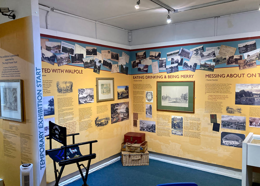 This image shows an interior view of a museum exhibition room with informational panels, pictures, texts on walls, a chair, and spotlights.
