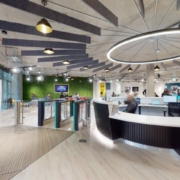 Modern office lobby with a reception desk, contemporary lighting, exposed ceiling, green wall accents, and people working or walking in the background.
