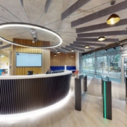 Modern office lobby with a sleek reception desk, overhead circular lighting, glass entrance gates, and bright, contemporary interior design elements.