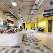Modern office space with a curved white counter, colorful walls, hexagonal floor patterns, exposed ceiling, and a person standing in the distance.