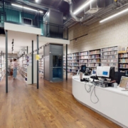 This is a modern library interior with bookshelves lining the space, a wooden floor, an upper walkway railing, and a person browsing books.