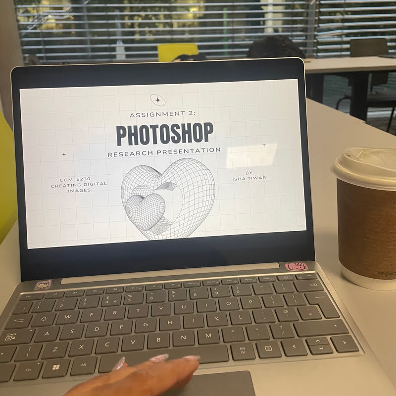 A laptop on a table displays a Photoshop research presentation. A hand is on the keyboard, with a coffee cup nearby.