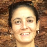 Close up of a person with dark brown hair and brown eyes against a brick wall