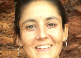 Close up of a person with dark brown hair and brown eyes against a brick wall