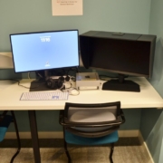 A computer workstation with dual monitors and audio equipment is set up in a room with a sign specifying its use for media tasks.