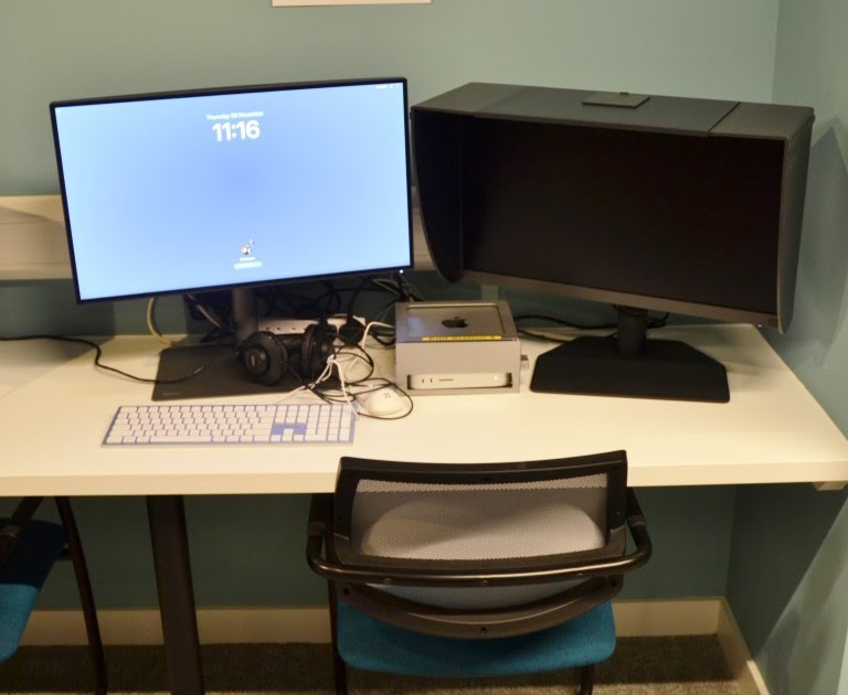 A computer workstation with dual monitors and audio equipment is set up in a room with a sign specifying its use for media tasks.