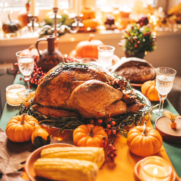 Thanksgiving table with roasted turkey, pumpkins, corn, and festive decorations, creating a warm and inviting holiday atmosphere with candles and lights.