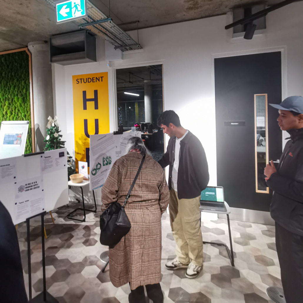 A group of people examines posters in a student hub area with a small Christmas tree and directional signs, suggesting an indoor event.