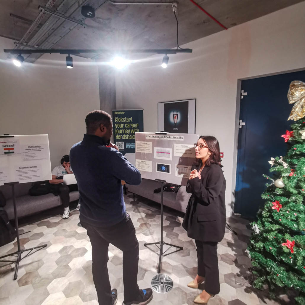 Two people discussing a presentation on cybersecurity. A person works on a laptop in the background. A decorated Christmas tree is nearby.