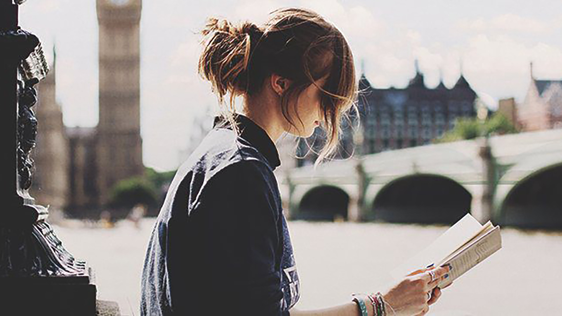 A person reads by the River Thames, with Big Ben and Westminster Bridge in the background, surrounded by a sunny, pleasant atmosphere.