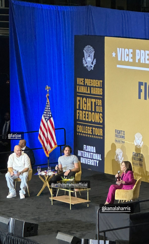 Three people sit on stage at a "Fight for Our Freedoms College Tour" event at Florida International University. An American flag is displayed.