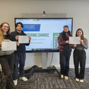 Four people holding certificates stand in front of a presentation screen displaying "John Cabot University" and the words "Engineering Change."