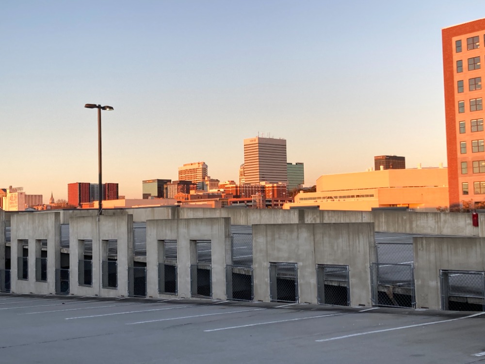 A concrete parking structure with a view of downtown Richmond, Virginia skyscrapers at sunset, under a clear sky.