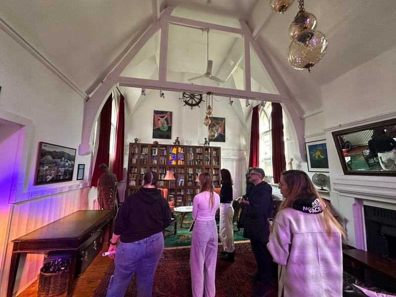 A group inside a historic library with vaulted ceilings, stained glass windows, and ornate decor, observing bookshelves and artwork.