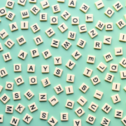 Scattered beige letter tiles on a light green background, forming partial words like "HAPPY" and "DAYS," creating a playful, abstract pattern.