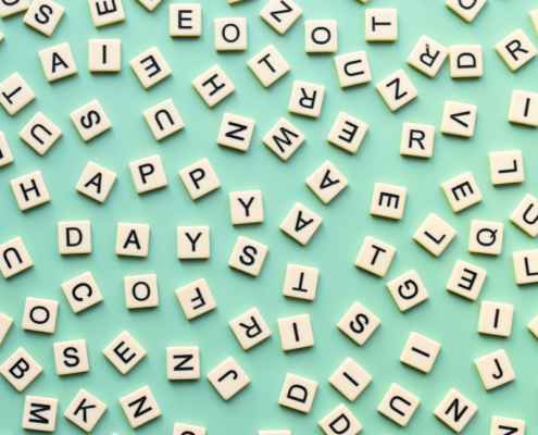Scattered beige letter tiles on a light green background, forming partial words like "HAPPY" and "DAYS," creating a playful, abstract pattern.