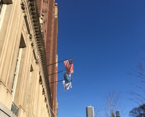 A historic Hilton hotel building with flags, clear sky, and a city skyline, including the Sears Tower, in the background.