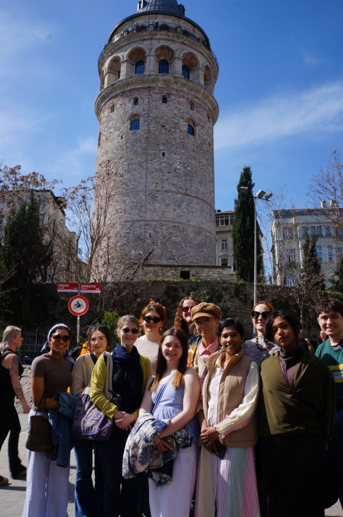 A group of people stands in front of the historic Galata Tower in Istanbul, under a clear blue sky.