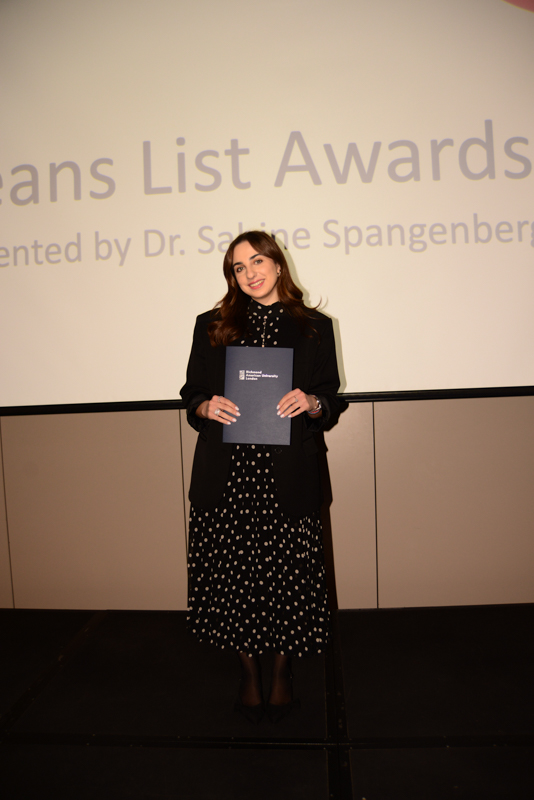 A person stands on stage holding a certificate at an awards event, with a presentation screen in the background.