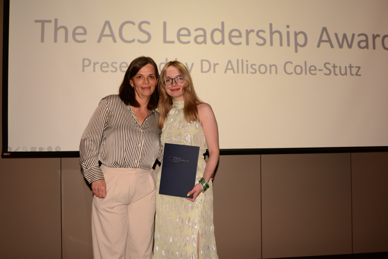 Two people stand in front of a screen displaying "The ACS Leadership Award," one holding a certificate.