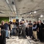 A group of people gather in an indoor setting with modern decor and informational posters, smiling for the photo.