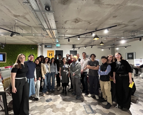 A group of people gather in an indoor setting with modern decor and informational posters, smiling for the photo.