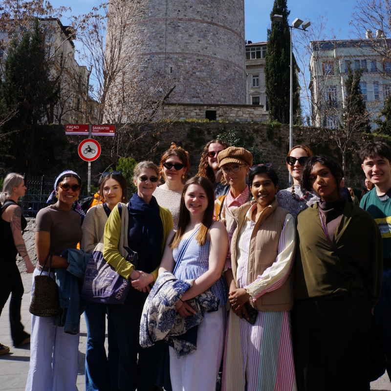 A group of people stands smiling in front of the Galata Tower in Istanbul, enjoying a sunny day and the historic atmosphere.