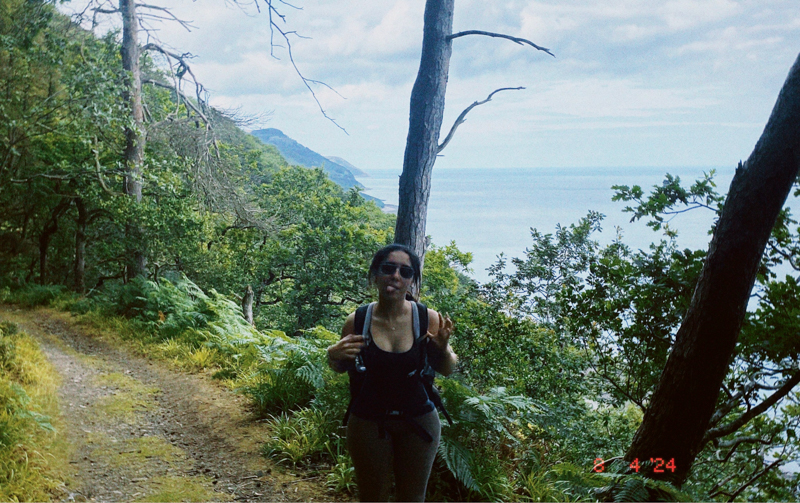 A person hiking along a scenic forested trail with ocean views. Lush greenery and coastal landscape create a calm, natural atmosphere.