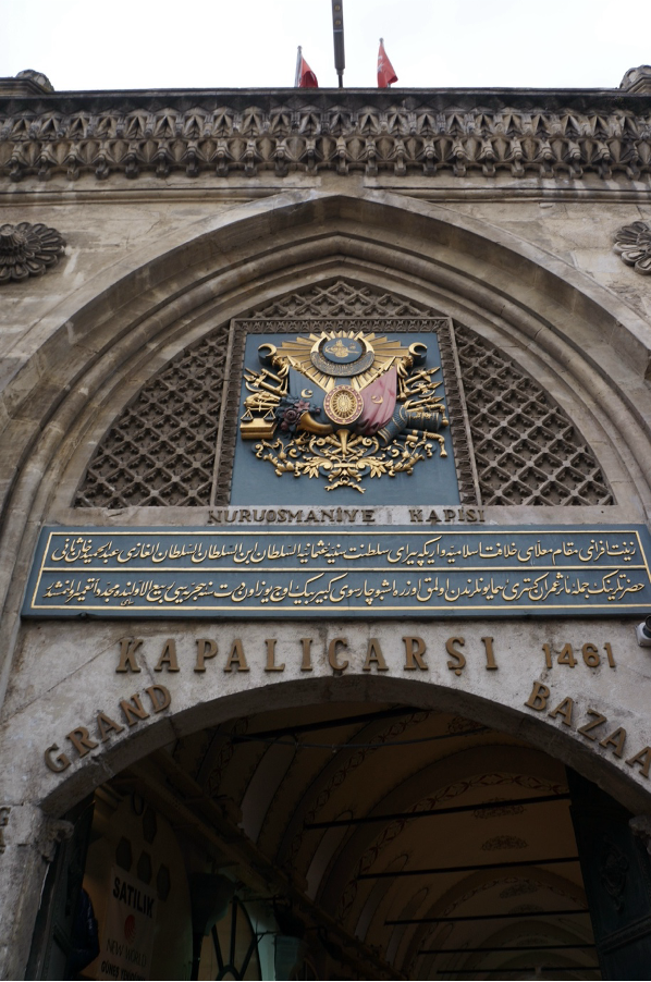 Entrance to the Grand Bazaar in Istanbul features intricate Ottoman emblem, decorative script, and archway detailing, marked "Kapalıçarşı 1461" and "Nuruosmaniye Kapısı."